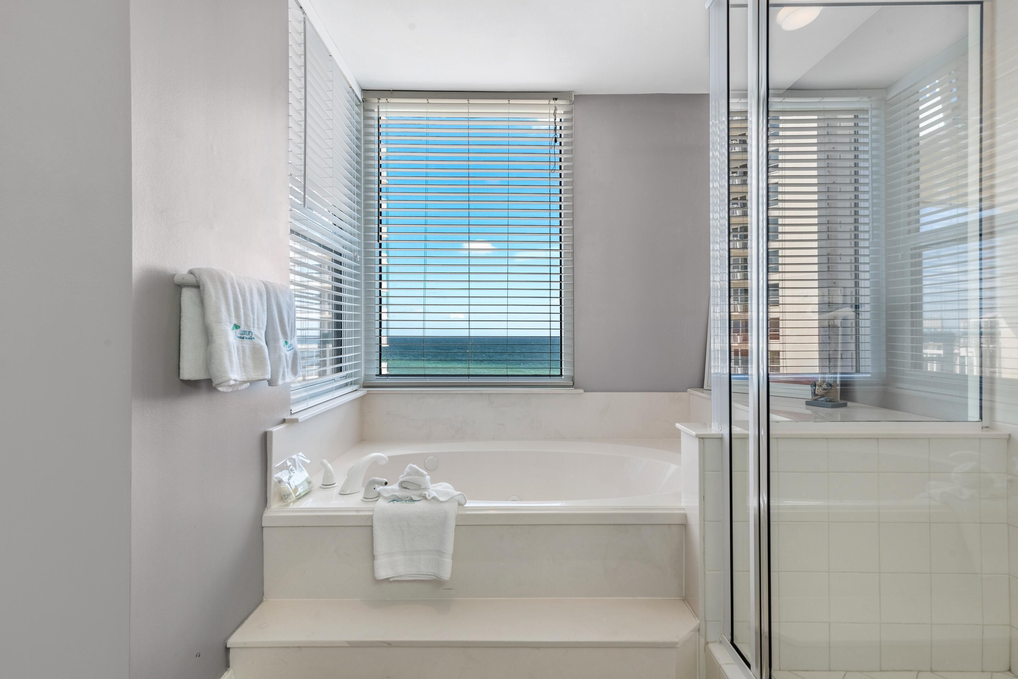 A modern bathroom with a bathtub, a shower area, and a window with blinds.