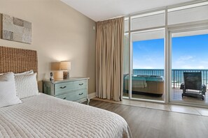 Un dormitorio con una cama grande, un aparador, una lámpara y vistas a un balcón con una silla y una mesa.