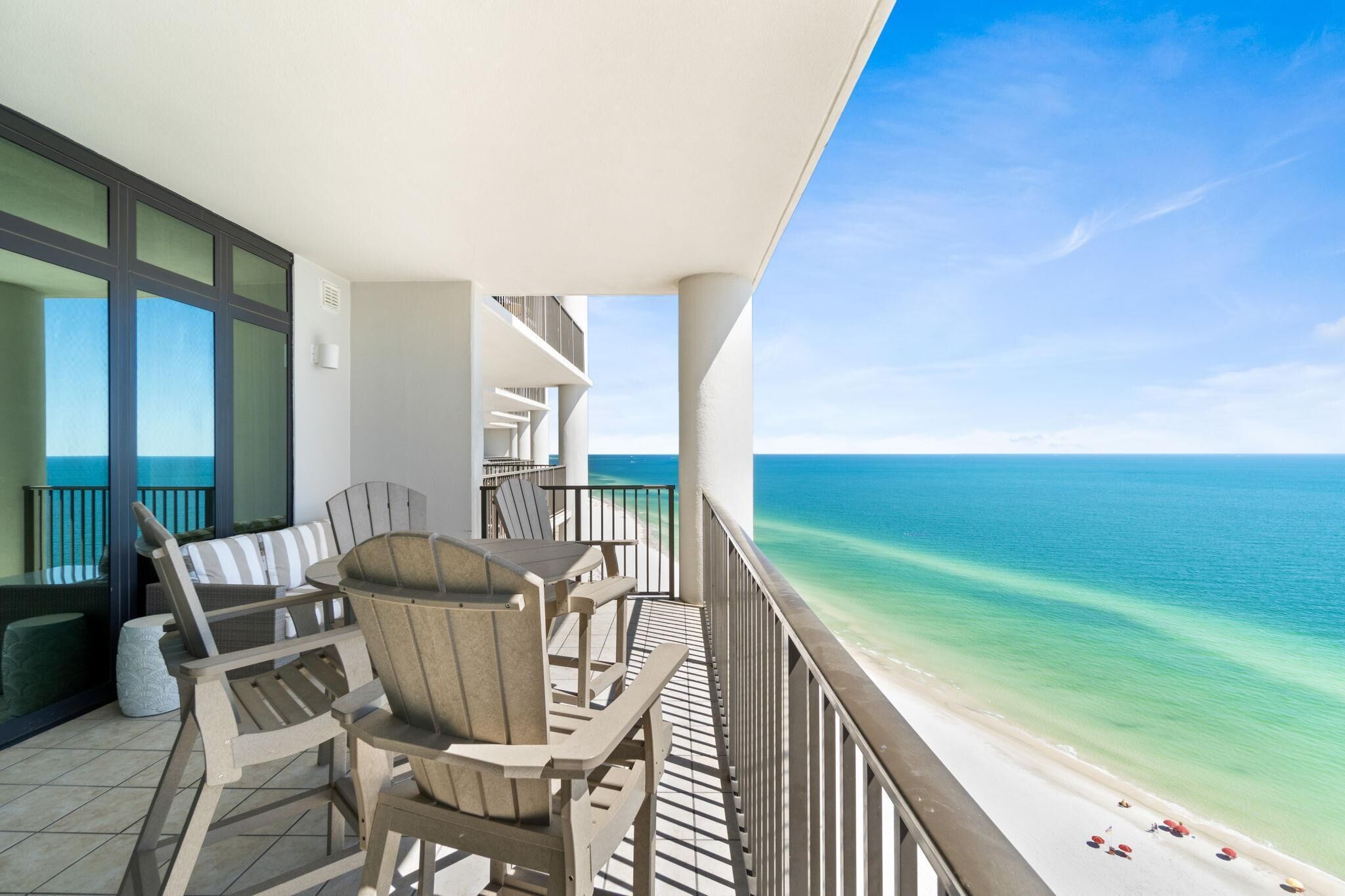 Een balkon met rieten stoelen en een tafel, met uitzicht op een strand met helder turquoise water.