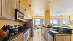 A kitchen with a stove, microwave, and refrigerator, leading to a dining area with a view. - La Playa 502 (Pensacola)