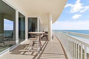 A balcony with a view of the ocean, furnished with tables and chairs, and a white railing.