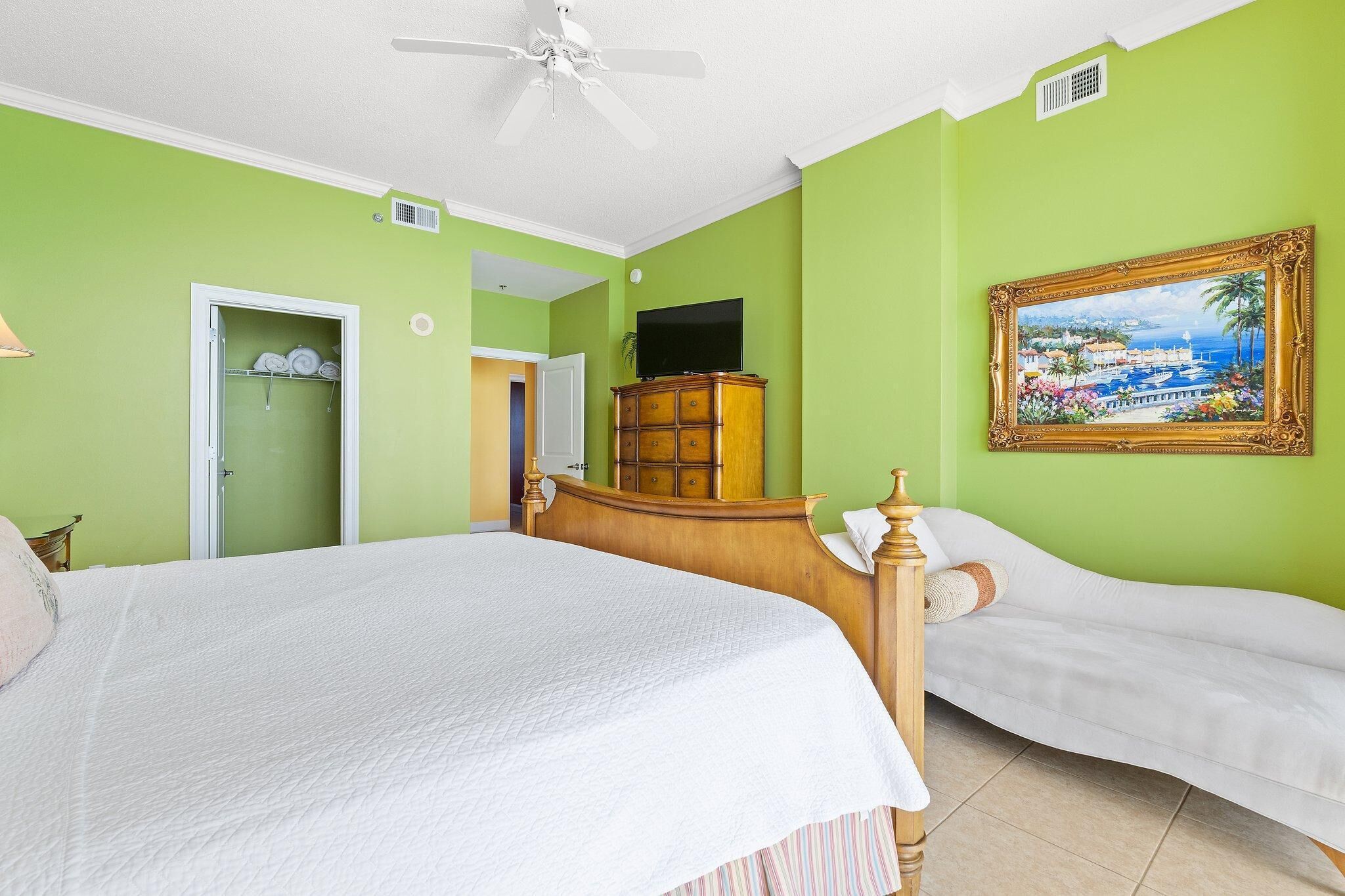 A bedroom with a large bed, a wooden dresser, a television, and a painting on the wall.