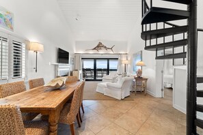 A spacious living area with a wooden dining table, wicker chairs, a white sofa, and a black spiral staircase. - Shipwatch B301 (Pensacola)