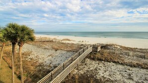 Una platja amb un camí de fusta que condueix a la riba, envoltada de dunes de sorra i vegetació escassa.