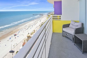 A balcony with a view of a beach, a wicker sofa, and a purple pillar. - Luxury 18th Floor 3 BR Condo Direct Oceanfront Wyndham Ocean Walk Resort Daytona Beach | 1804 (Daytona Beach)