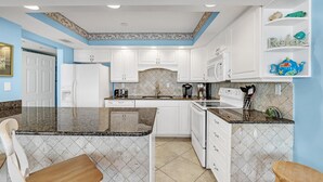 A kitchen with white cabinets, granite countertops, and a microwave. There is a sink, a stove, and a coffee maker. - Seaspray West 603- Gulf Front (Pensacola)