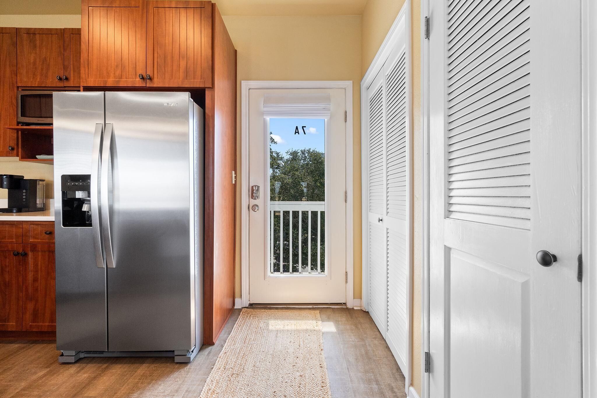 Una cocina con armarios de madera, un refrigerador de acero inoxidable y una puerta blanca que da a un balcón.