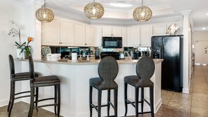 A kitchen with a central island, bar stools, a black refrigerator, and hanging wicker pendant lights. - Phoenix West 2005 (Orange Beach)