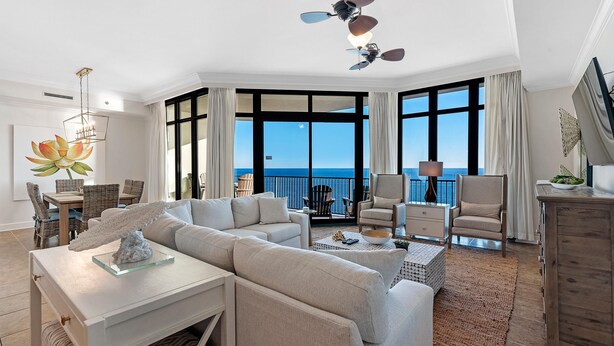 A spacious living room with a large window overlooking the ocean, a ceiling fan, and a dining area with wicker furniture. - Phoenix West 2005 (Orange Beach)
