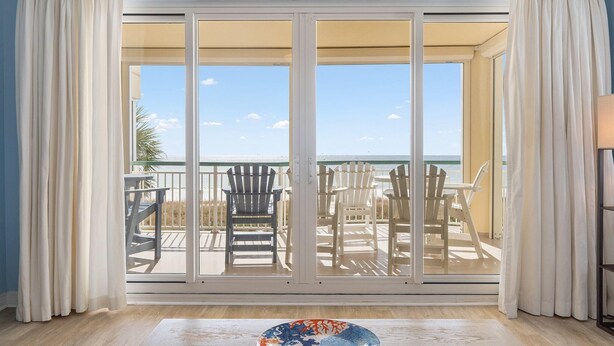 Quarto com uma grande porta de correr de vidro que dá para um deck externo com cadeiras e uma mesa.
