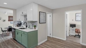 Une cuisine moderne avec des meubles blancs, un îlot central vert et un coin repas comprenant une table et des chaises.