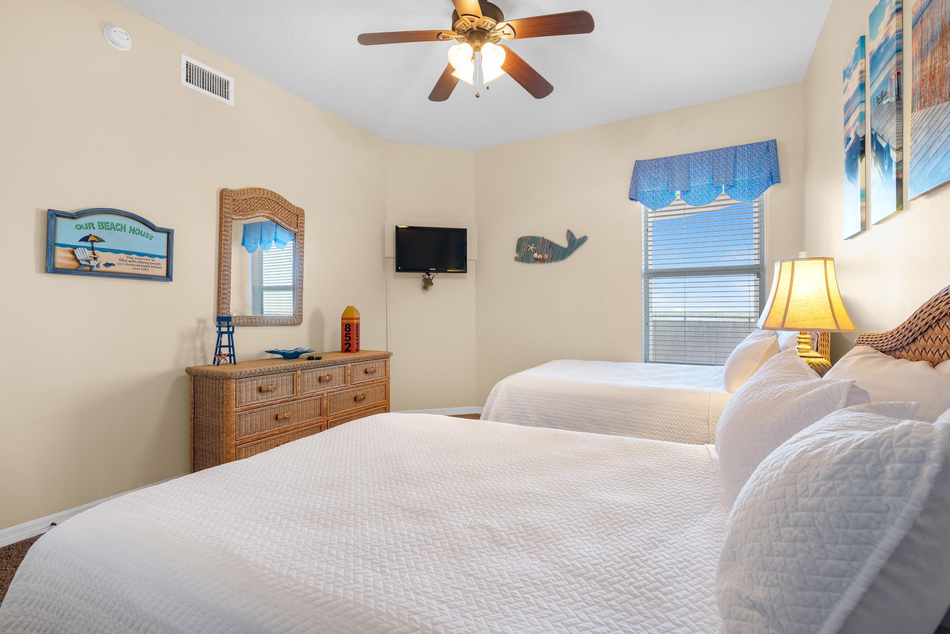 A bedroom with two beds, a ceiling fan, a TV, a dresser, and a window with blinds.