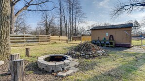 A rustic outdoor area with a stone fire pit, a wooden fence, and a small building with a door and windows.