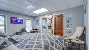 A bedroom with a bed, a desk, a chair, a TV, and a door.