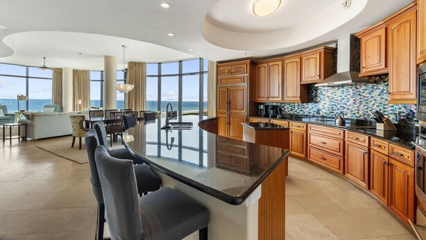A modern kitchen with a large island, wooden cabinets, and a view of the ocean. - Capri 202 + Free Seasonal Beach Service (Pensacola)