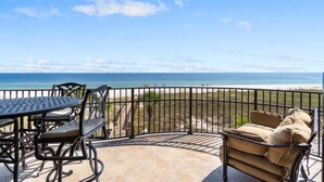 A balcony with a table and chairs, overlooking a beach. - Capri 202 + Free Seasonal Beach Service (Pensacola)