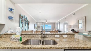 A modern kitchen with granite countertops, stainless steel sink, and a ceiling fan. - Windemere 1003 (Pensacola)