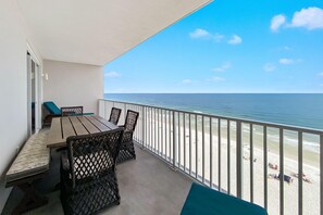 Un balcón con vista a la playa, una mesa, sillas y un banco.