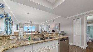 A modern kitchen with granite countertops, white cabinetry, and a built-in dishwasher. - Windemere 1003 (Pensacola)
