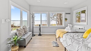 A modern bedroom with a large window, a bed with a yellow pillow, a bedside table, and a plant. - Whidbey Waterview Getaway: Nature, Deers, Pet & Family Friendly (Clinton)