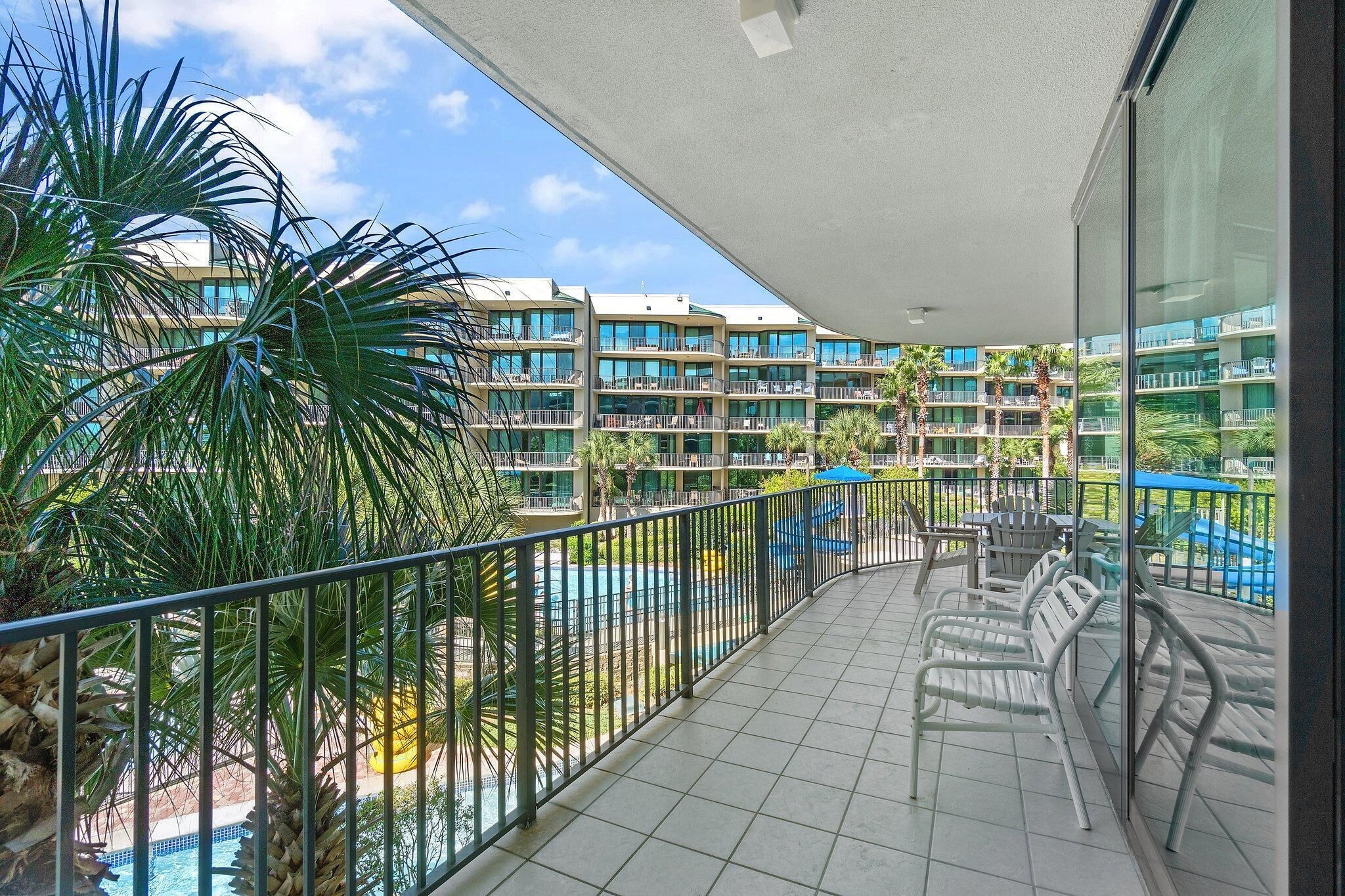 Ein Balkon mit Blick auf einen Swimmingpool, Palmen und ein mehrstöckiges Gebäude mit Balkonen.