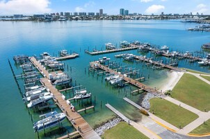 Uma marina com várias docas e barcos, rodeada por água e um horizonte urbano distante.