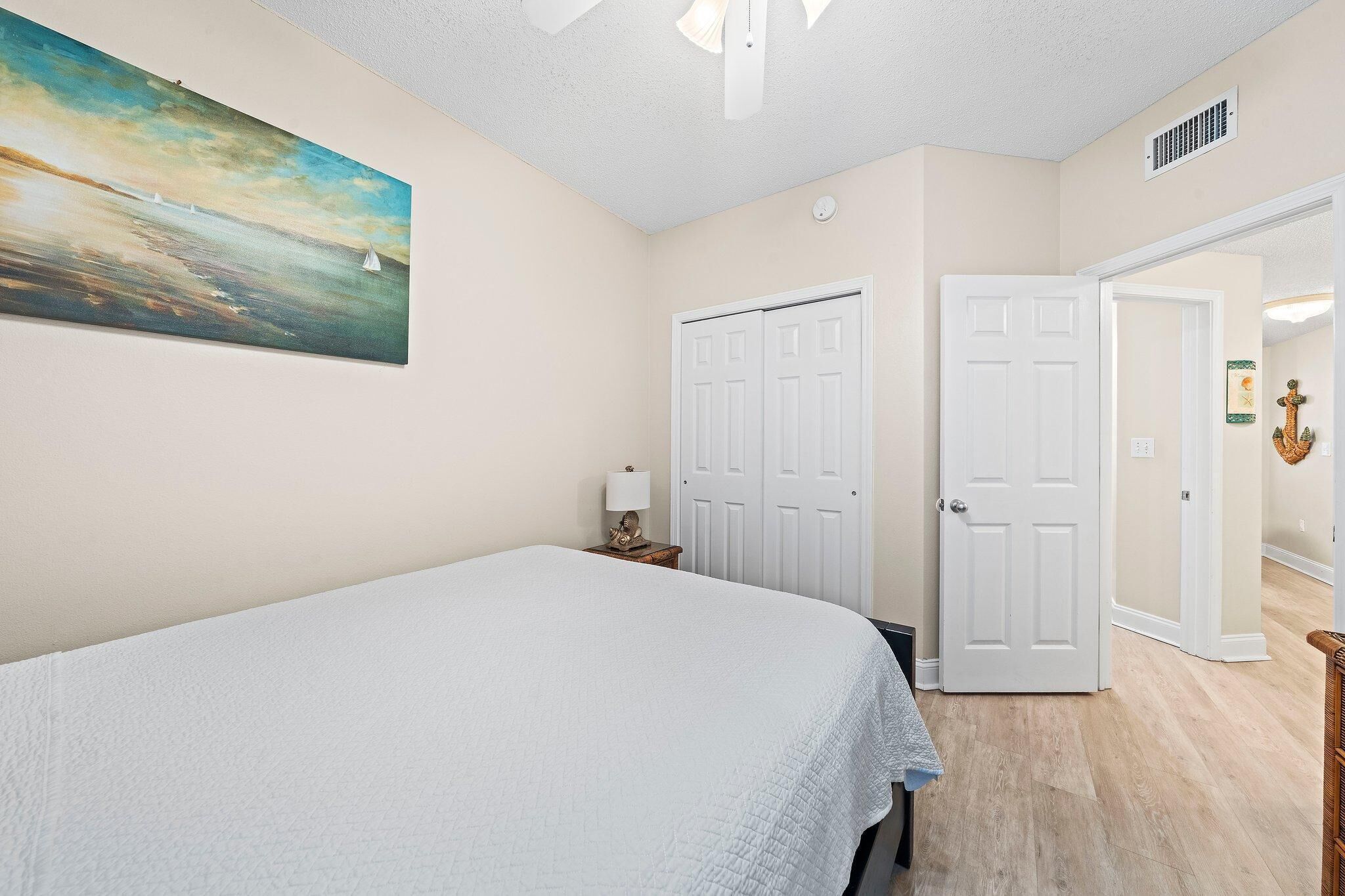 A bedroom with a bed, a painting, a door, and a hallway.
