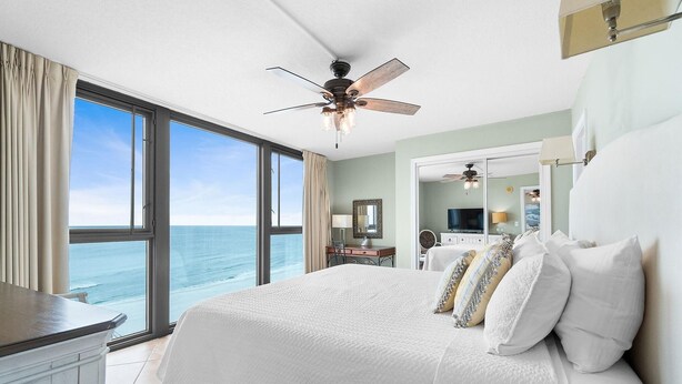 A bedroom with a large bed, a ceiling fan, and a view of the ocean. - Perdido Towers West 906 (Pensacola)