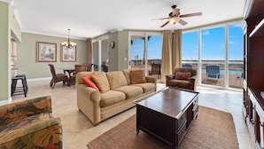 A spacious living room with a beige sofa, a coffee table, and a view of a pool through large windows. - Seaspray West 105- Gulf Front (Pensacola)