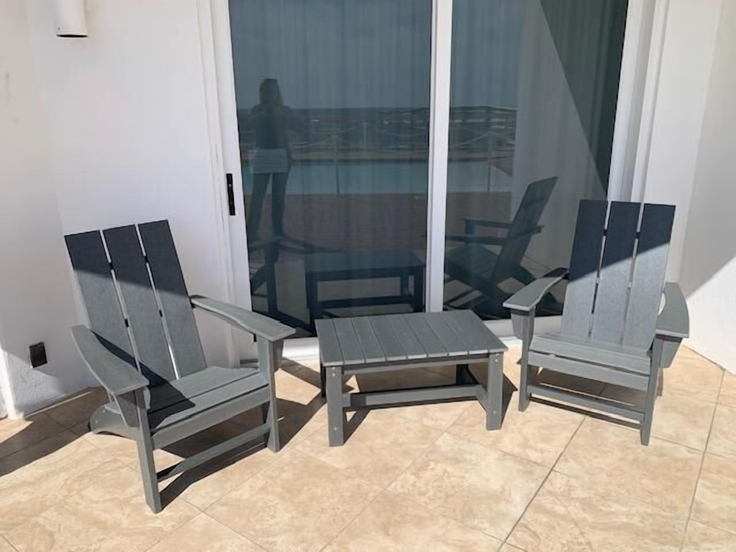 A patio area with two Adirondack chairs and a small table, a sliding glass door, and a view of the cityscape.