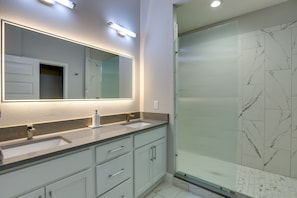 Une salle de bain avec deux lavabos, un grand miroir et une douche fermée par une paroi de verre.