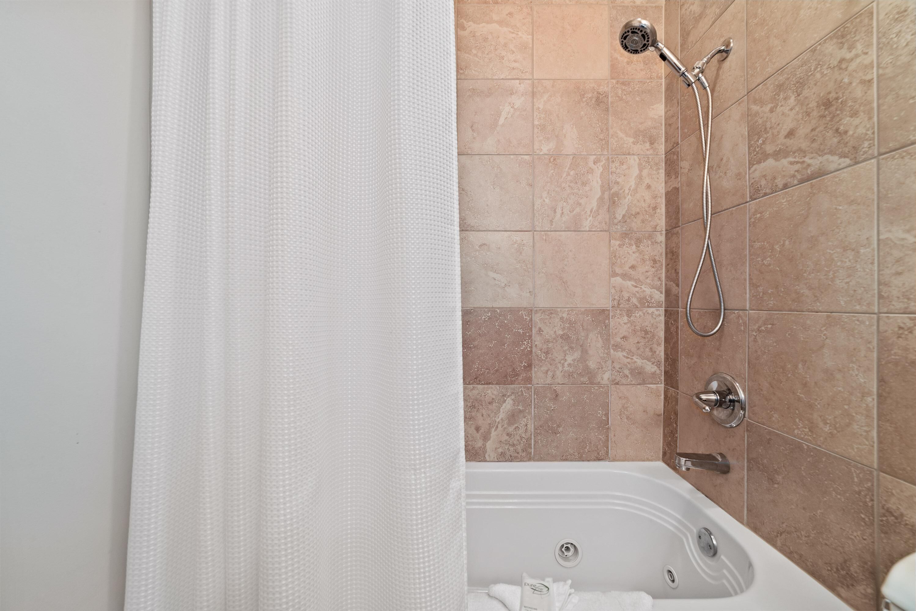 A bathroom with a bathtub, a showerhead, and beige tiled walls.