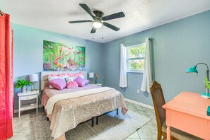 Un dormitorio con cama, ventilador de techo, ventana y escritorio.