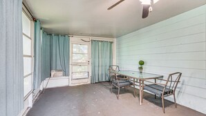 Et værelse med et bord, fire stole, en ventilator i loftet og et vindue med gardiner.