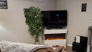 A living room with a brown sofa, a flat-screen TV, a fireplace, a potted plant, and motivational wall art. - Charming Cozy Suite In Langford. (Victoria)