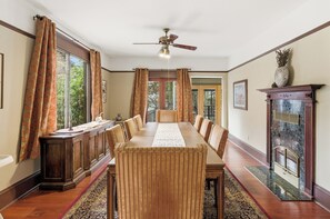 A dining room with a long table, chairs, a wooden cabinet, and a fireplace.