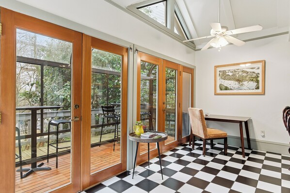 A room with a checkered floor, a ceiling fan, a table with a chair, and a view of the outdoors through large glass doors.