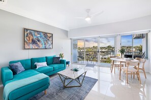 A modern living room with a teal sofa, a coffee table, and a balcony with a view.