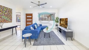 A modern living room with a blue sofa, a small round table, a TV, and a ceiling fan.