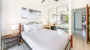 A hotel bedroom with a large bed, a ceiling fan, a nightstand with a lamp, a bedside table, a large mirror, and a view of the outside.