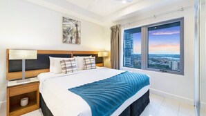 A modern hotel room with a large bed, a city view, a ceiling fan, and a nightstand with a lamp.