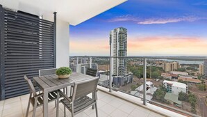 A balcony with a table and chairs, a potted plant, and a view of a tall building and surrounding cityscape.