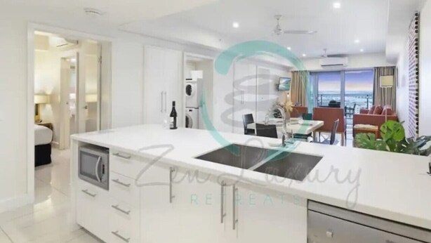 A modern kitchen with a central island, white cabinetry, and a view of the living area.
