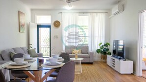 A modern living room with a dining area, a sofa, a TV, and a balcony. - Zen Nest: Cozy  ~ Lawn ~ Minimalist (Nightcliff)