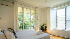 A bedroom with a bed, a bedside lamp, a potted plant, and a window with blinds. - Zen Nest: Cozy  ~ Lawn ~ Minimalist (Nightcliff)