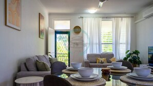 A modern living room with a round glass table set for dining, two sofas, a TV, and a balcony with a view. - Zen Nest: Cozy  ~ Lawn ~ Minimalist (Nightcliff)