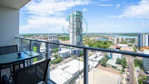 A balcony with a table and chairs, overlooking a cityscape with modern buildings and a body of water.