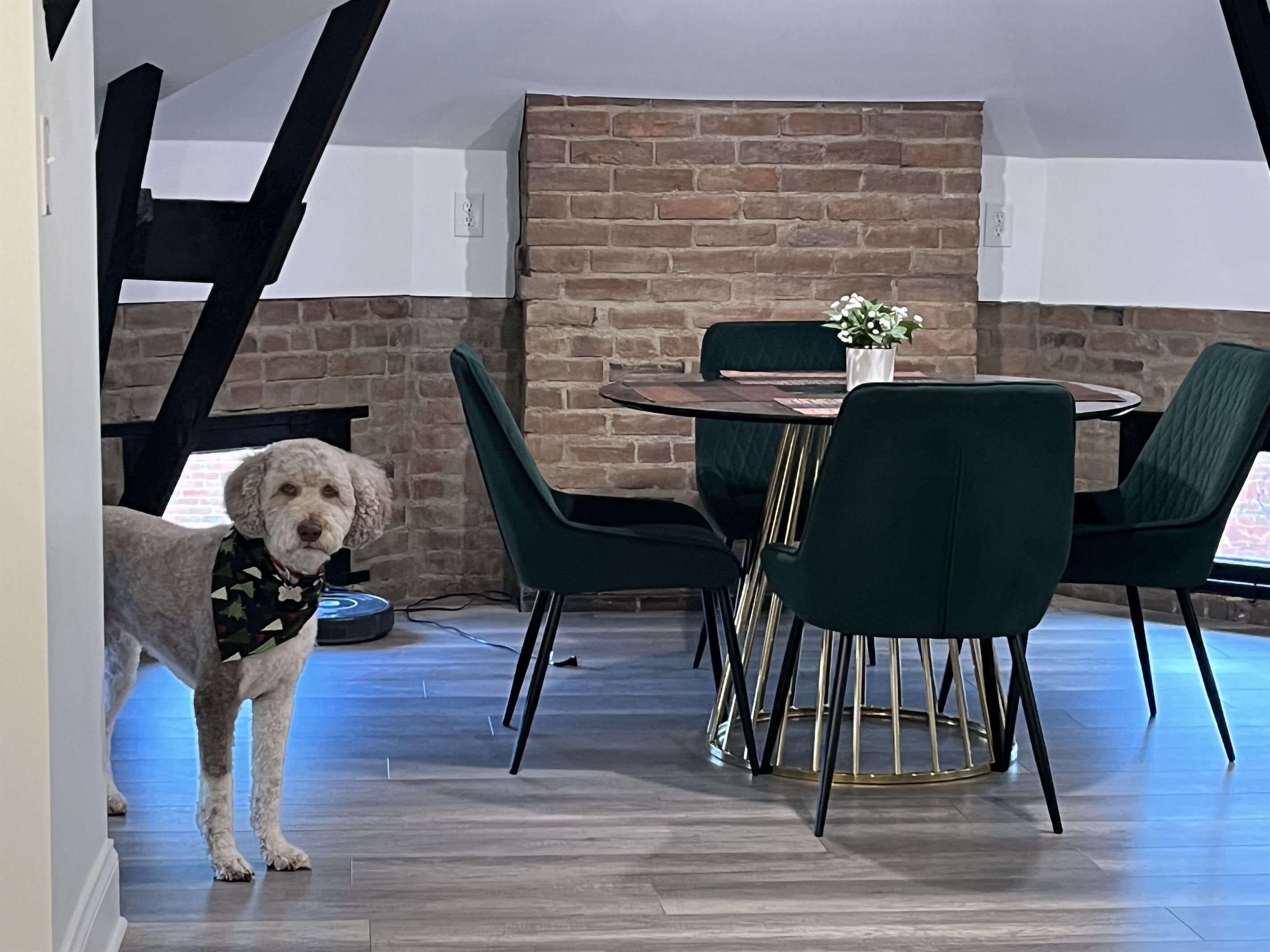 A dining area with a brick wall, a round table, and green chairs.