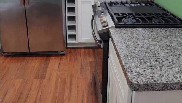 A kitchen with a stainless steel refrigerator, a stove, and white cabinets.