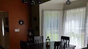 A dining room with a dark wooden table and chairs, a chandelier, and a window with sheer curtains.
